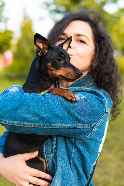 Junge Frau mit ihrem kleinen Hund draußen. Black and Tan Zwergpinscher Hündin mit Besitzer in einem Park