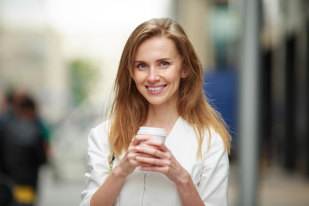 Junge Frau mit Kaffee zum Mitnehmen in der Straße. Unscharf gestellter Hintergrund.