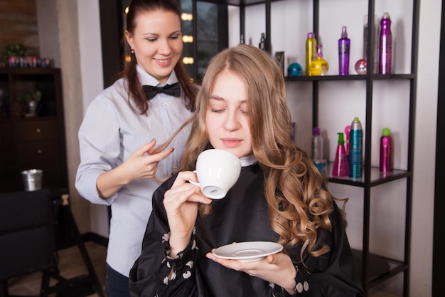 Junge Frau mit Kaffeetasse und Friseur mit Haarspray
