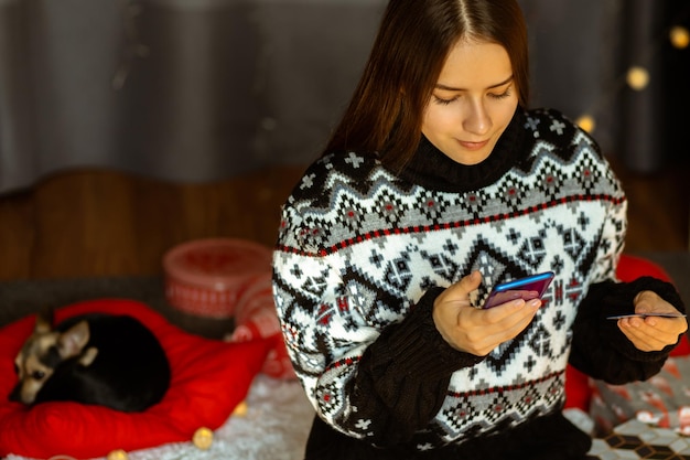Junge Frau mit kleinem Hund kauft Rabatte für Weihnachtsgeschenke per Kreditkarte über den Online-Shop von zu Hause aus