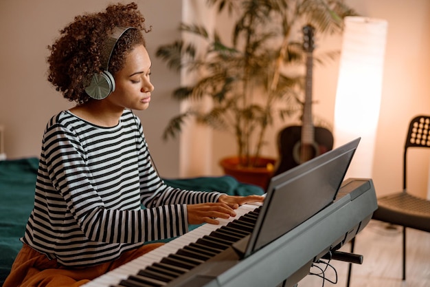 Junge Frau mit Kopfhörern, die zu Hause Synthesizer spielt