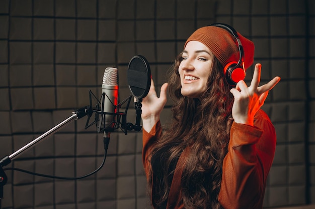 Junge Frau mit Kopfhörern singt emotional im Mikrofon im Tonaufnahmestudio Star-Talent bereitet Showstudio-Aufnahmen vor Schalldichter Raum für professionelle Gesangsaufnahmen