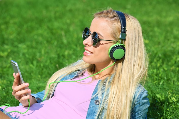 Junge Frau mit Kopfhörern und Smartphone, die Musik auf Gras hört