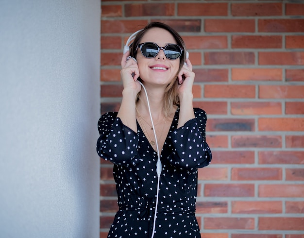 Junge Frau mit Kopfhörern und Sonnenbrille auf Mauer