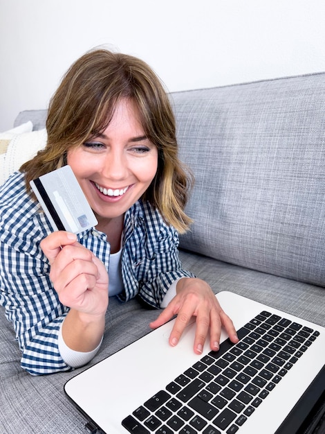 Junge Frau mit Kreditkarteneinkauf über Laptop, während sie zu Hause sitzt stockfoto