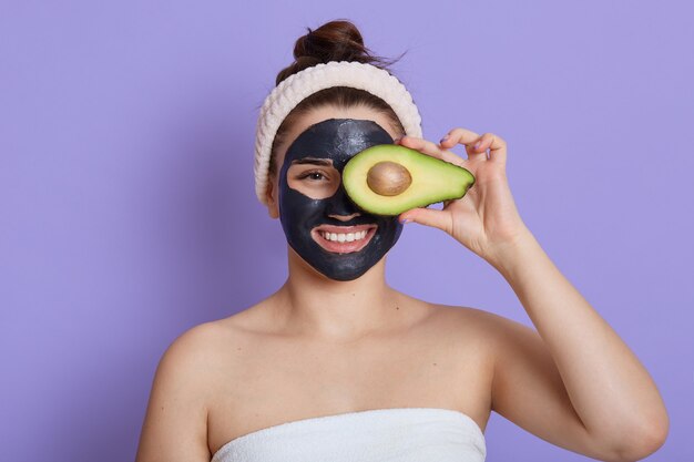 Junge Frau mit Lächeln, die Avocado hält und Auge damit bedeckt