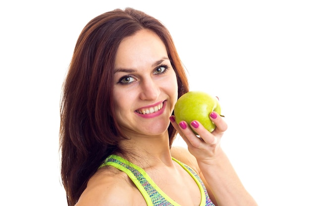 Junge Frau mit langen braunen Haaren in farbigem Sporttop mit grünem Apfel im Studio