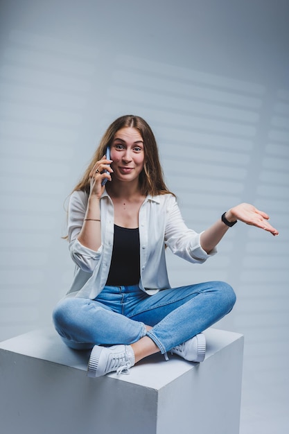 Junge Frau mit langen brünetten Haaren trägt ein weißes Hemd und Jeans am Telefon sprechen Eine Frau in Jeans und einem einfachen weißen Hemd mit einem Mobiltelefon Weißer Hintergrund Kopie Raum