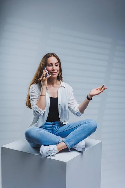 Junge Frau mit langen brünetten Haaren trägt ein weißes Hemd und Jeans am Telefon sprechen Eine Frau in Jeans und einem einfachen weißen Hemd mit einem Mobiltelefon Weißer Hintergrund Kopie Raum