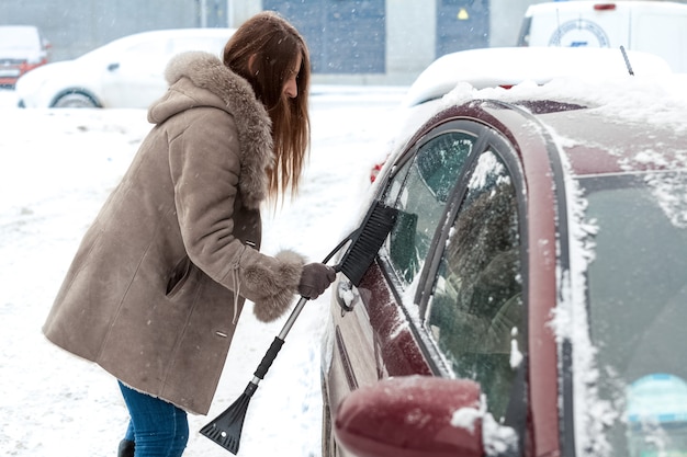 Junge Frau mit langen Haaren, die Auto nach Schneesturm säubert