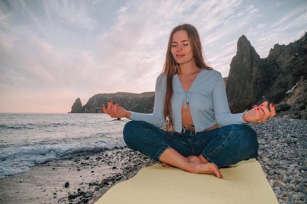 Foto junge frau mit langen haaren, die sich bei einem warmen sonnenuntergang im freien auf einer yogamatte am meer dehnt