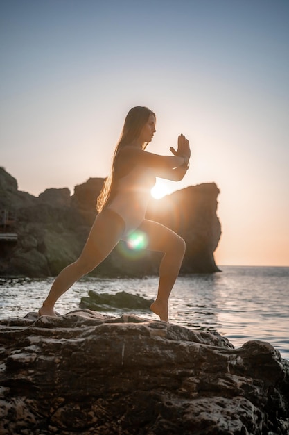 Junge Frau mit langen Haaren im weißen Badeanzug und Boho-Stil-Armbändern, die im Freien auf Yogamatte üben