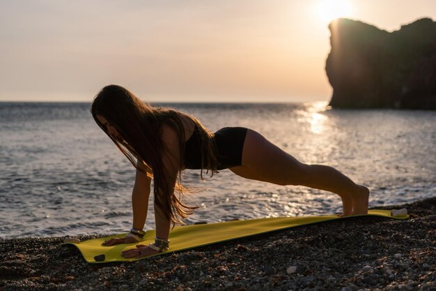 Junge Frau mit langen Haaren in schwarzem Badeanzug und Armbändern im Boho-Stil, die im Freien auf einer Yogamatte üben