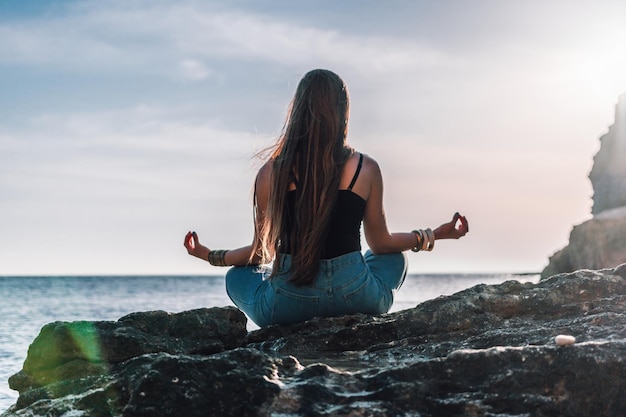 Junge Frau mit langen Haaren in schwarzem Badeanzug und Armbändern im Boho-Stil, die im Freien auf einer Yogamatte üben