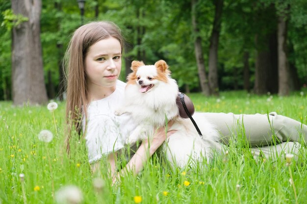 Junge Frau mit langen Haaren liegt mit einem pommerschen Hund auf dem Rasen im Park