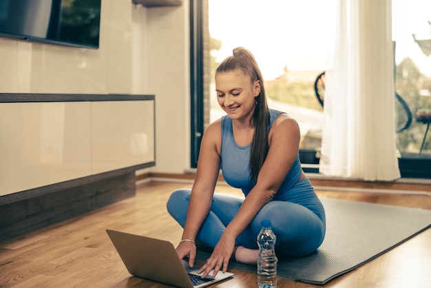 Junge Frau mit Laptop beim morgendlichen Fitnesstraining zu Hause.