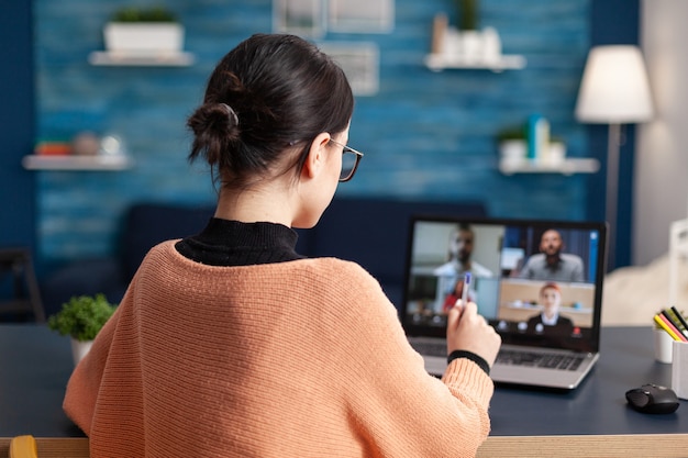 Junge Frau mit Laptop-Computer im Gespräch mit Kollegen über Schulkommunikationsprojekt während der Videokonferenz der Universität. Student in der E-Learning-Fernausbildung während der Coronavirus-Quarantäne