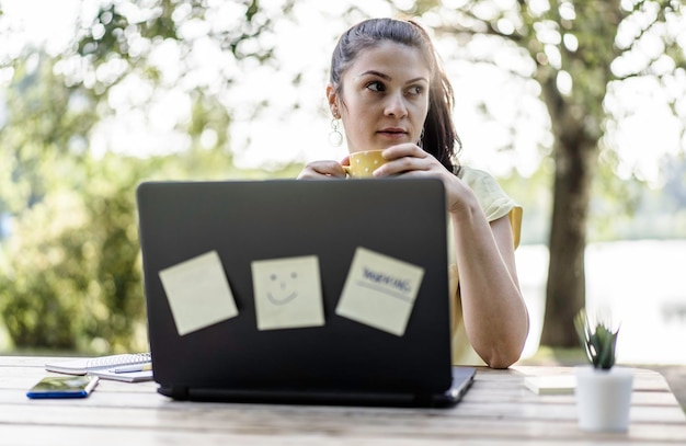 Junge Frau mit Laptop-Computer im öffentlichen Park Millennial-Freiberuflerin, die remote arbeitet und sich Notizen in einem Stadtpark macht Technologie- und Remote-Arbeitskonzept Verwendung von technischen Geräten im Freien