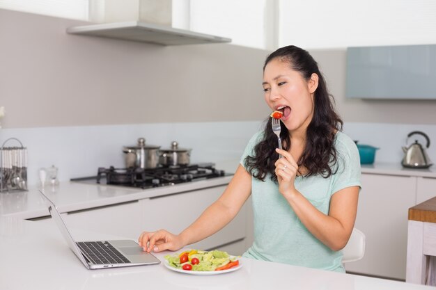 Junge Frau mit Laptop Salat in der Küche essend