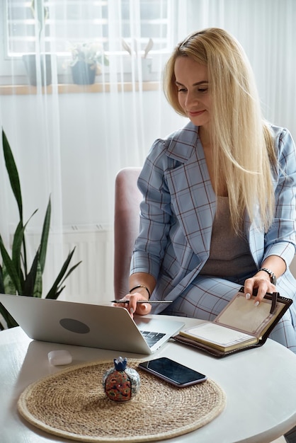 Junge Frau mit Laptop sitzt zu Hause am Schreibtisch und arbeitet zu Hause