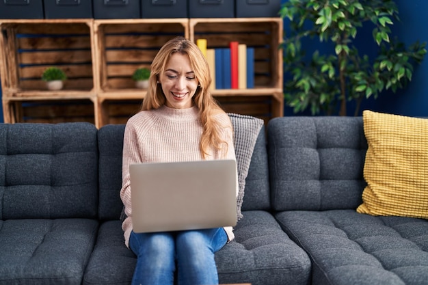 Junge Frau mit Laptop sitzt zu Hause auf dem Sofa