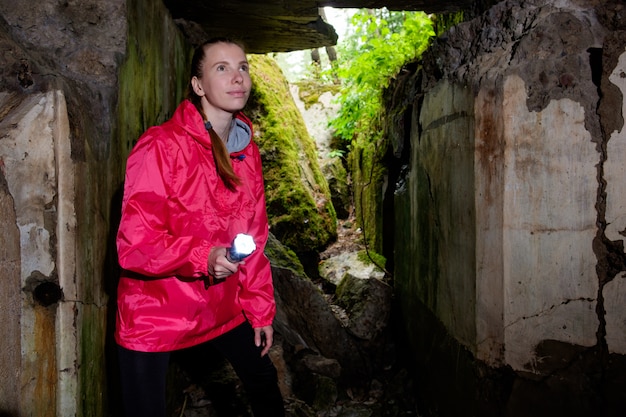 Junge Frau mit Laterne, getragen im roten Wassermantel, erforscht alte Festungshöhle