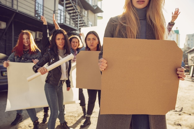 Junge Frau mit leerem Plakat vor Menschen, die auf der Straße gegen Frauenrechte und Gleichberechtigung protestieren. Treffen über Probleme am Arbeitsplatz, männlicher Druck, häusliche Gewalt, Belästigung. Exemplar.