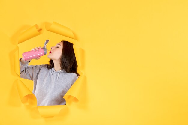 junge Frau mit leerer Flasche Wasser auf zerrissenem gelbem Papierhintergrund Athlet fit Indoor-Fitnessstudio