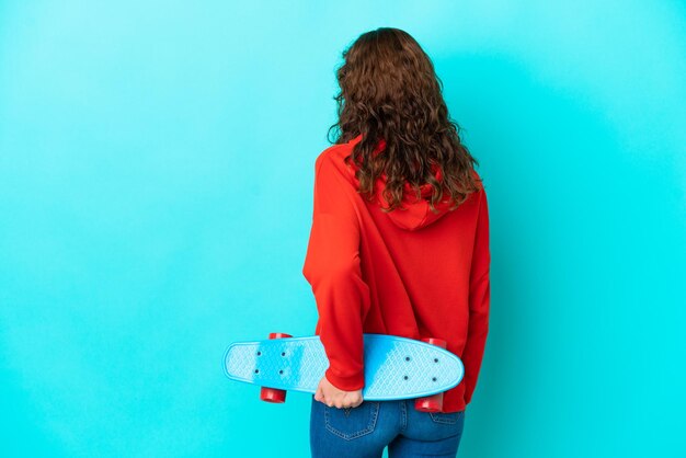 Junge Frau mit lockigem Haar isoliert auf blauem Hintergrund mit einem Schlittschuh in Rückenlage