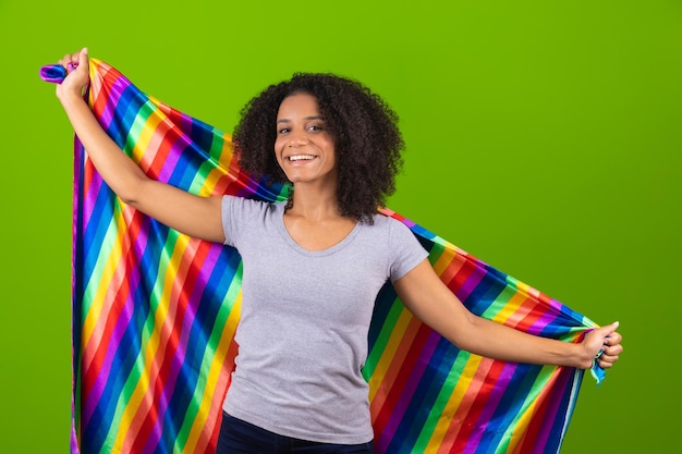 Junge Frau mit lockigem Haar mit Regenbogenfahne isoliert auf grünem Hintergrund LGBT-Konzept