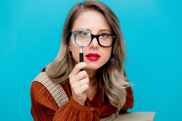 Junge Frau mit Lupe und Büchern auf Blau