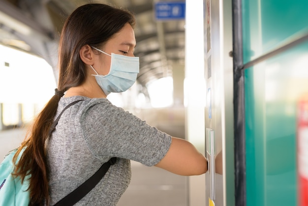 Junge Frau mit Maske, die Aufzugsknopf mit Ellbogen drückt, um die Ausbreitung des Koronavirus an der Skytrain-Station zu verhindern