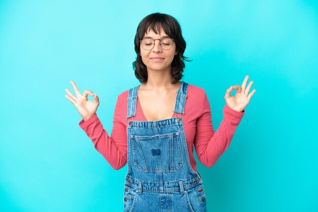 Junge Frau mit Overall isoliert Hintergrund in Zen-Pose