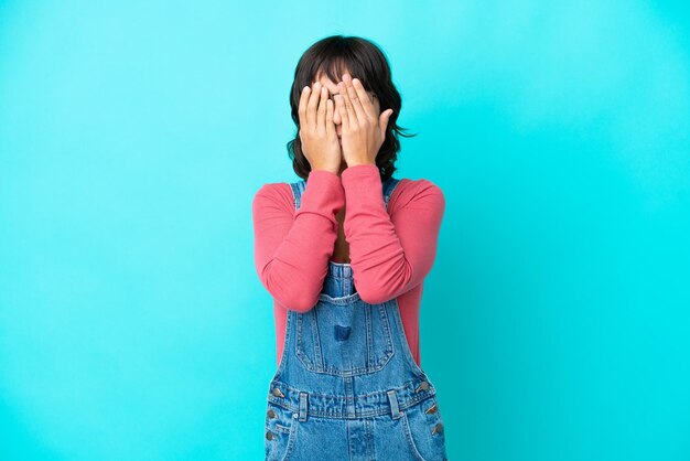 Junge Frau mit Overall isolierter Hintergrund, der die Augen mit den Händen bedeckt