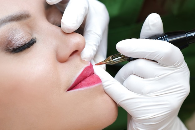 Junge Frau mit Permanent Make-up auf den Lippen im Kosmetiksalon. Natürlicher grüner Hintergrund. Nahaufnahme