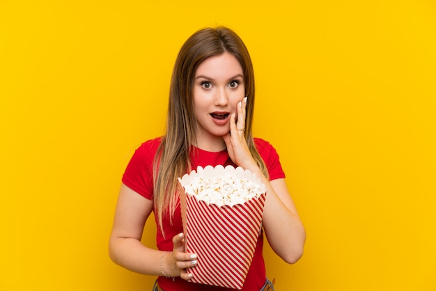 Junge Frau mit Popcorn über rosa Wand mit Überraschung und entsetztem Gesichtsausdruck