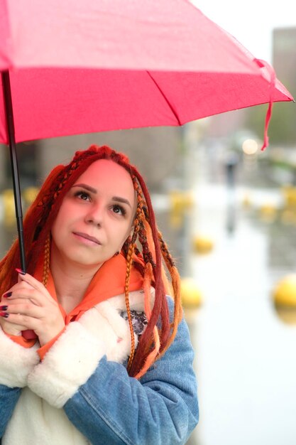 Foto junge frau mit regenschirm auf der straße positive junge frau in warmer kleidung lächelt, während sie auf der straße der stadt steht