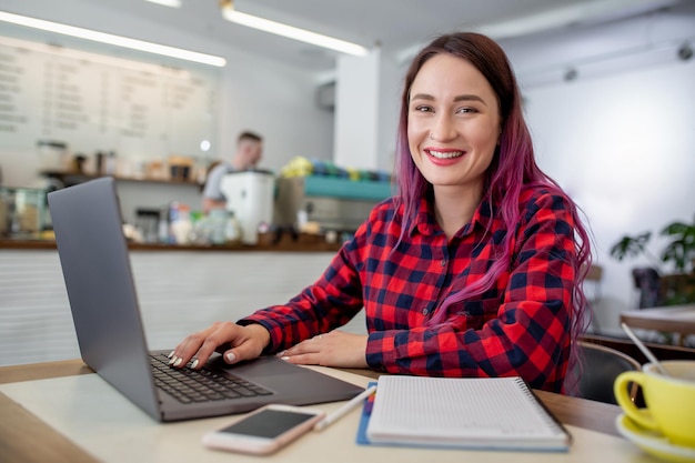 Junge Frau mit rosa Haaren mit Laptop-Computer sitzt im Café intelligente Studentin, die o...