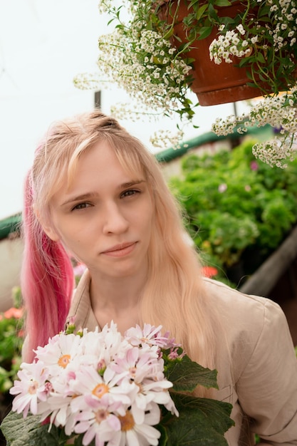 Junge Frau mit rosa und blonden Haaren, die rosa Blumen im Garten hält