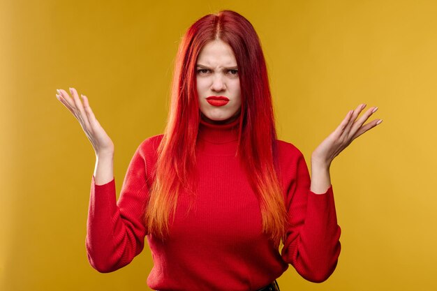 Junge Frau mit roten Haaren, die den Kopf mit den Händen auf gelbem Hintergrund hält