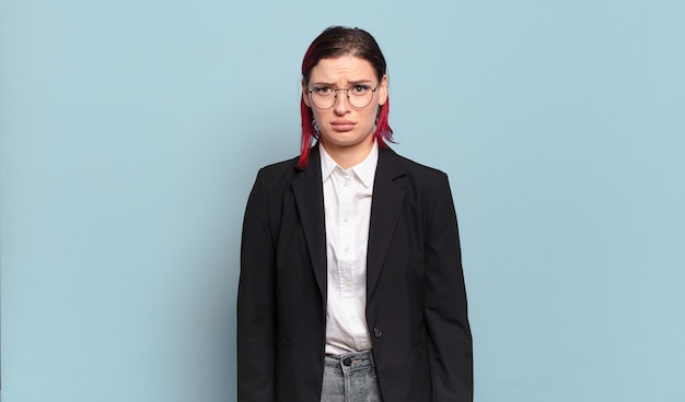 Junge Frau mit roten Haaren, die sich traurig und weinerlich mit einem unglücklichen Blick fühlt und mit einer negativen und frustrierten Haltung weint