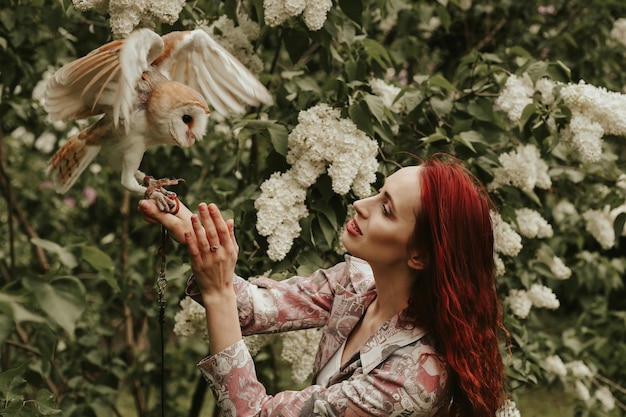 Junge Frau mit roten Haaren in einem lila Garten mit einer Eulenschleiereule