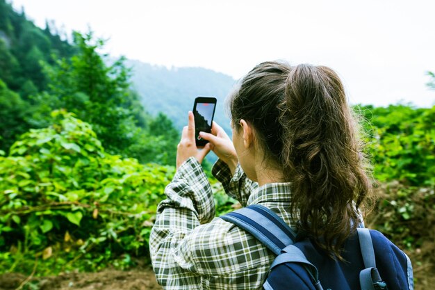 Foto junge frau mit rucksack, die mit ihrem handy ein video von einer schönen aussicht dreht