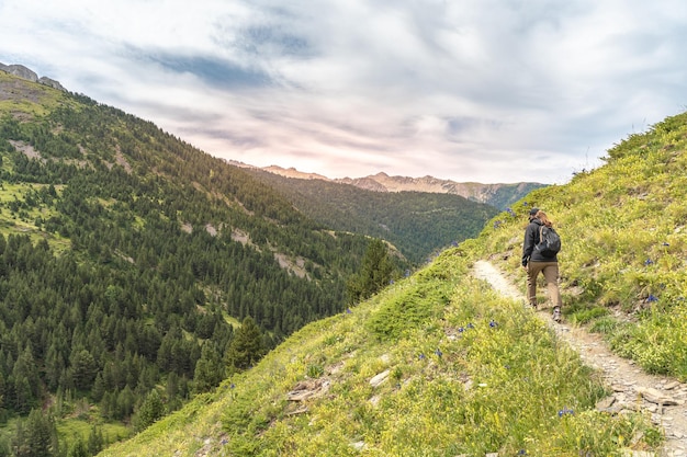 Junge Frau mit Rucksack klettert auf die Spitze des Berges gegen die Entdeckungsreise bei Sonnenuntergang