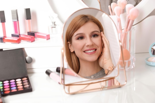 Junge Frau mit schönem Make-up, die drinnen im Spiegel schaut