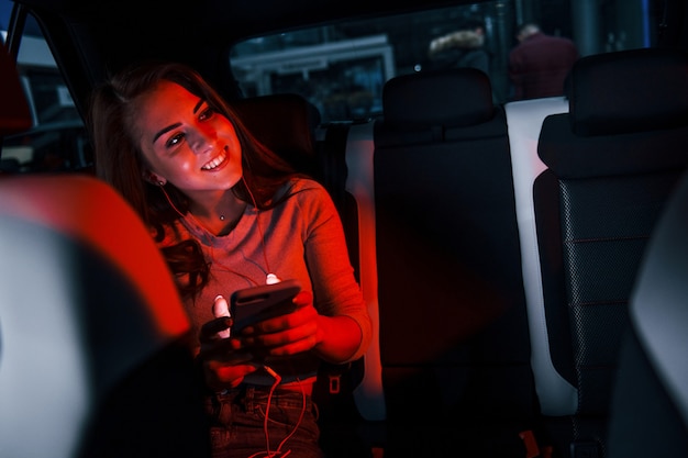 Junge Frau mit Smartphone ist im brandneuen modernen Automobil.