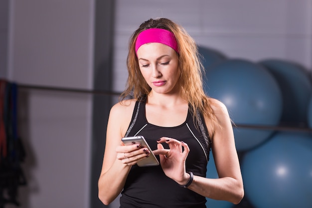 Junge Frau mit Smartphone und Fitness-Tracker im Fitnessstudio