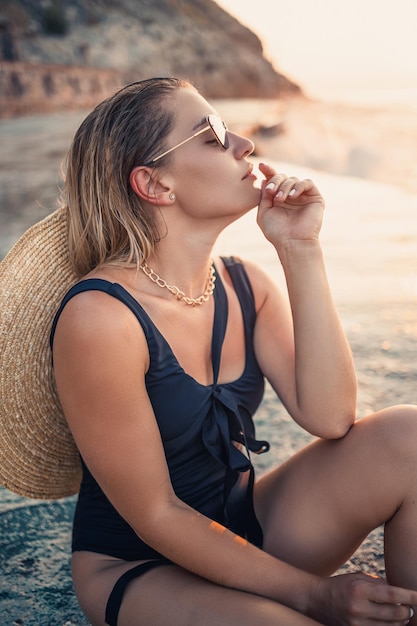 Junge Frau mit Sonnenbrille ruht am Meer schlank in einem schwarzen Badeanzug Selektiver Fokus