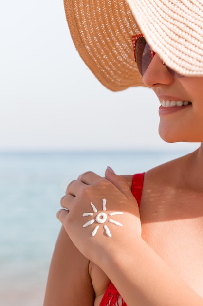 Junge Frau mit Sonnenform an der Hand, die aus Sonnencreme am Strand gefertigt wurde