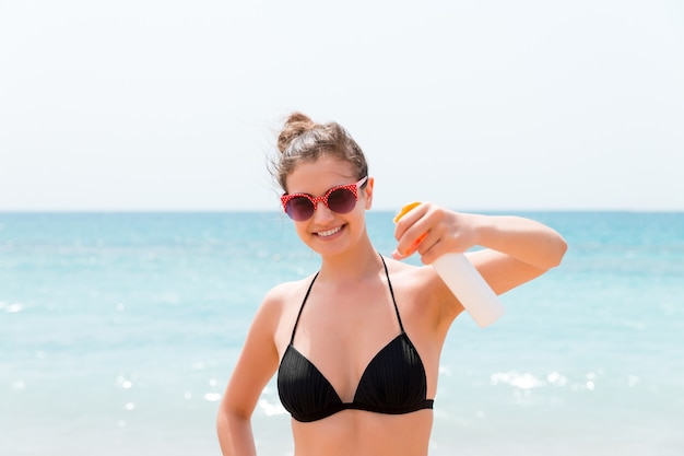 Junge Frau mit Sonnenschutzspray für Körper am Strand.